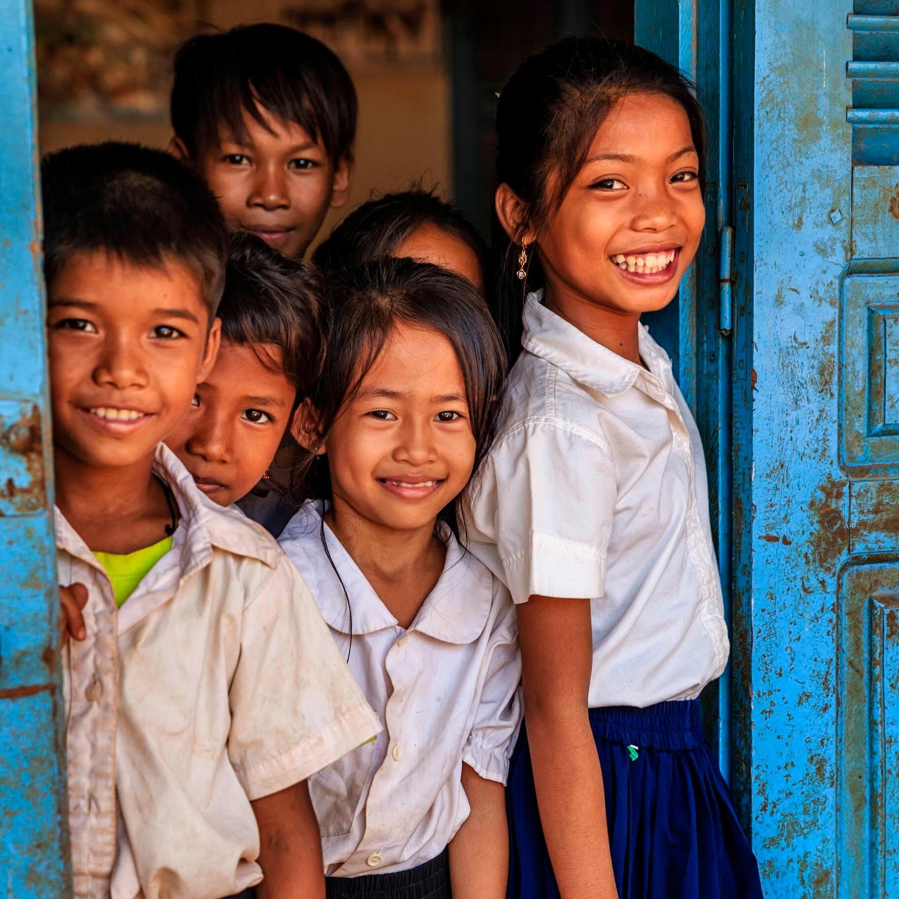 A group of children in school uniforms standing in a doorway and smiling.